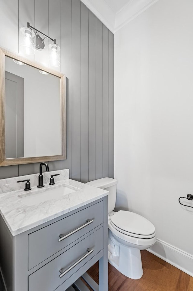 half bath featuring toilet, ornamental molding, wood finished floors, and vanity