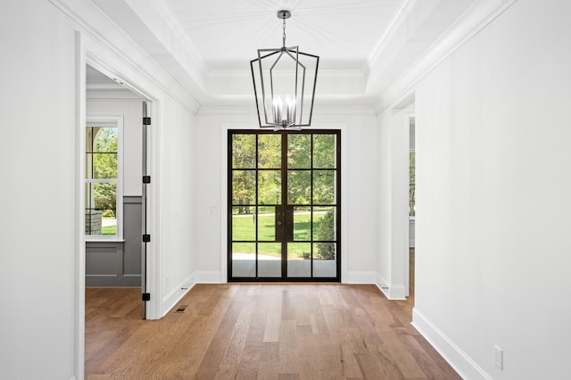 doorway to outside with ornamental molding, a tray ceiling, a notable chandelier, and wood finished floors