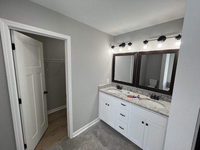 bathroom featuring double vanity, baseboards, toilet, and a sink