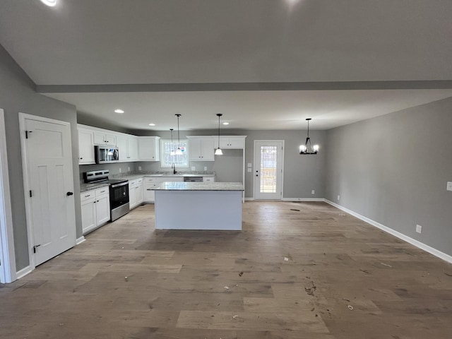 kitchen featuring light wood finished floors, white cabinets, appliances with stainless steel finishes, a center island, and an inviting chandelier