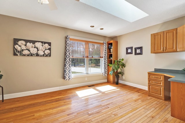 unfurnished office with light wood-style flooring, a skylight, a ceiling fan, visible vents, and baseboards