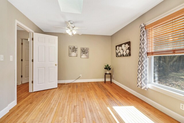 unfurnished room featuring baseboards, a skylight, a ceiling fan, and light wood-style floors