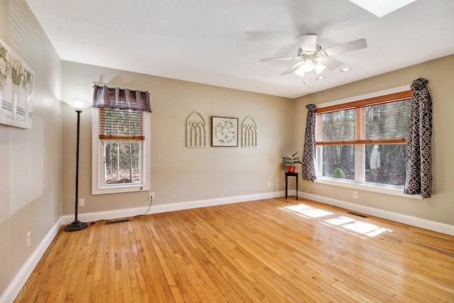 empty room with visible vents, light wood-type flooring, a ceiling fan, and baseboards