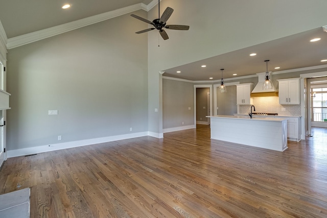 unfurnished living room with a sink, baseboards, wood finished floors, and crown molding