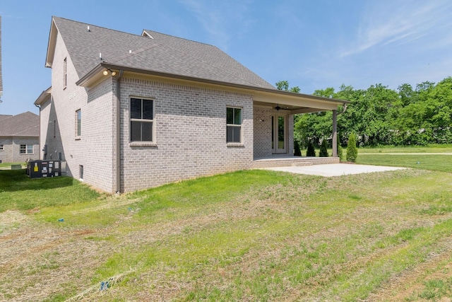 rear view of property featuring roof with shingles, brick siding, a yard, and a patio