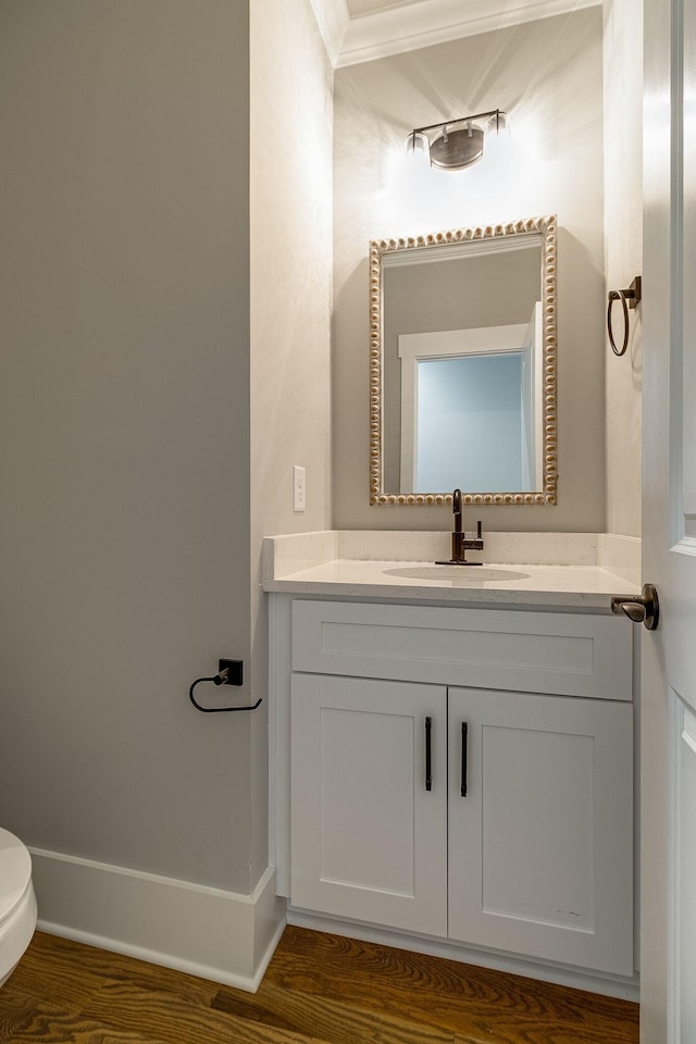 half bathroom with toilet, wood finished floors, and vanity