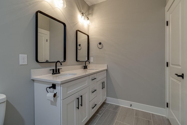 bathroom with double vanity, a sink, toilet, and baseboards