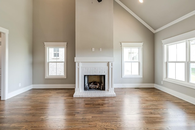 unfurnished living room with ornamental molding, a brick fireplace, wood finished floors, high vaulted ceiling, and baseboards