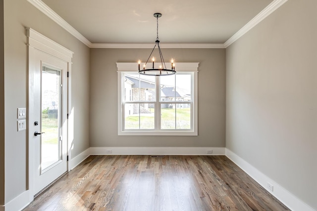 unfurnished dining area with an inviting chandelier, baseboards, crown molding, and wood finished floors