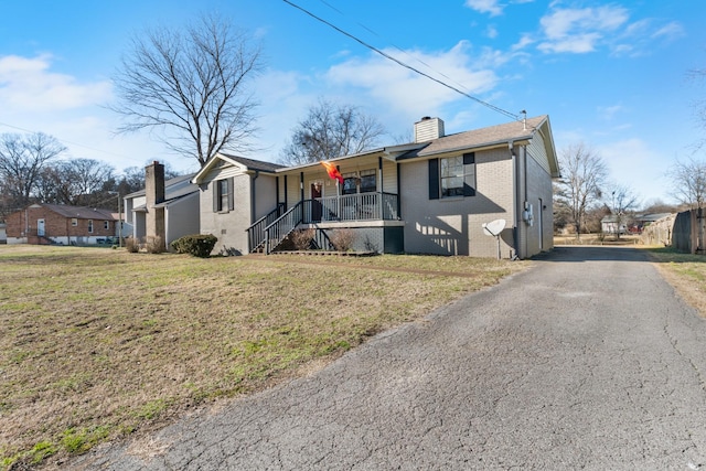 view of front facade featuring a chimney, aphalt driveway, covered porch, a front lawn, and brick siding