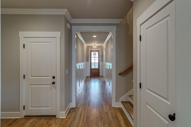 hallway featuring a decorative wall, a wainscoted wall, wood finished floors, stairway, and crown molding