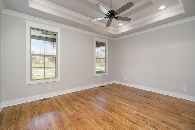 empty room with light wood-style flooring, a tray ceiling, baseboards, and ornamental molding