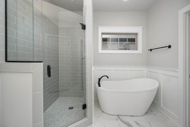 full bathroom with a stall shower, wainscoting, marble finish floor, a freestanding bath, and a decorative wall