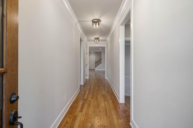 hallway with ornamental molding, stairway, light wood-type flooring, and baseboards