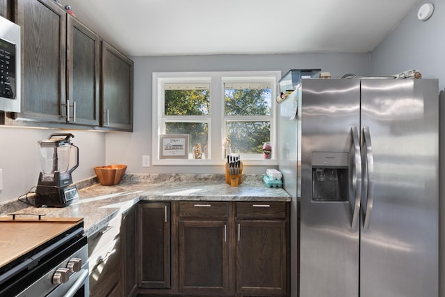 kitchen with appliances with stainless steel finishes, dark brown cabinetry, and light stone countertops