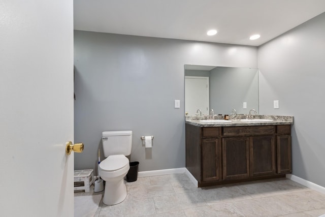 full bathroom with toilet, double vanity, baseboards, and a sink