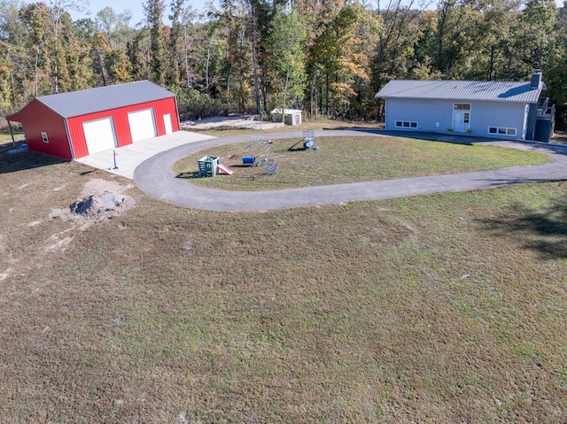 view of yard featuring driveway, a detached garage, a view of trees, and an outbuilding