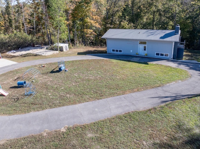 view of front of property featuring metal roof, a chimney, a front yard, and a view of trees