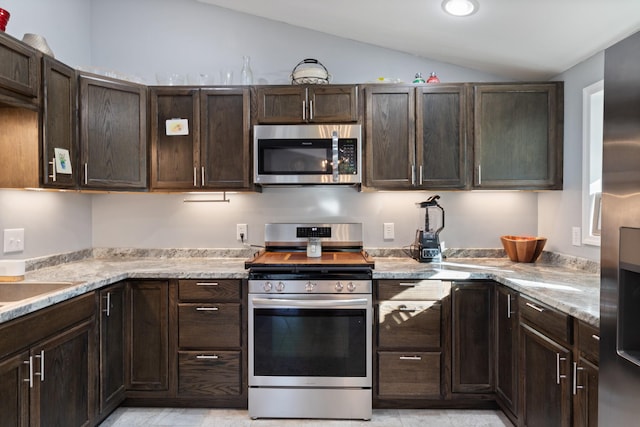 kitchen featuring lofted ceiling, stainless steel appliances, dark brown cabinets, and light stone countertops