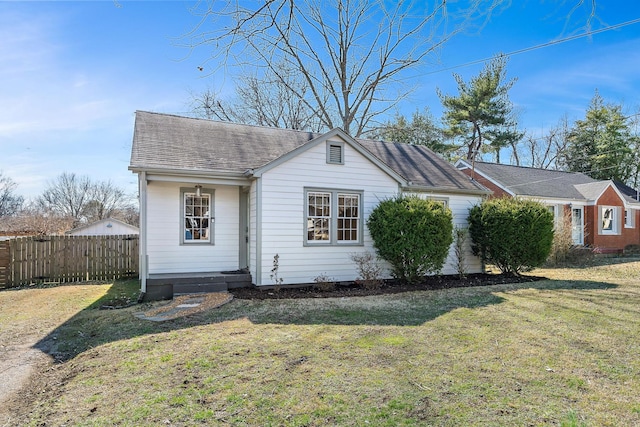 view of front facade featuring a shingled roof, fence, and a front yard