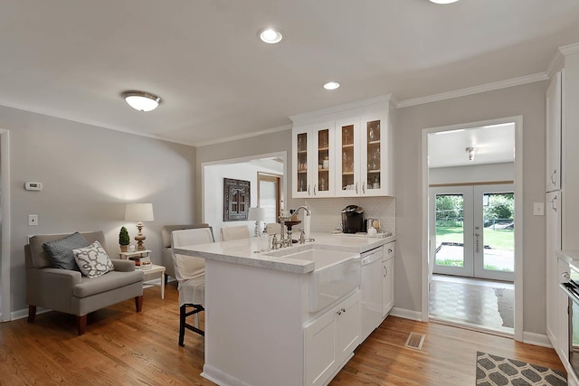 kitchen featuring a breakfast bar area, glass insert cabinets, white dishwasher, a sink, and a peninsula