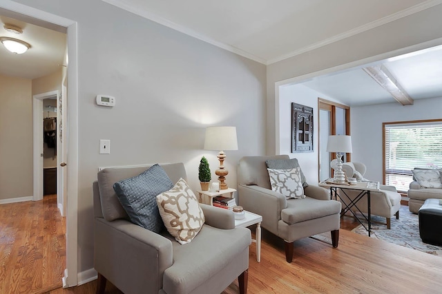 sitting room with ornamental molding, beam ceiling, light wood-style flooring, and baseboards