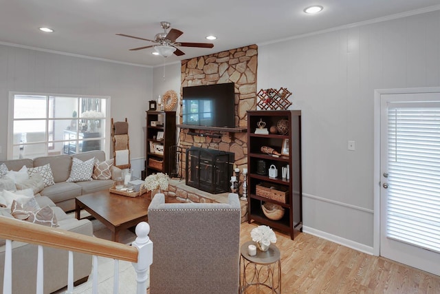 living area with a stone fireplace, wood finished floors, a ceiling fan, baseboards, and crown molding