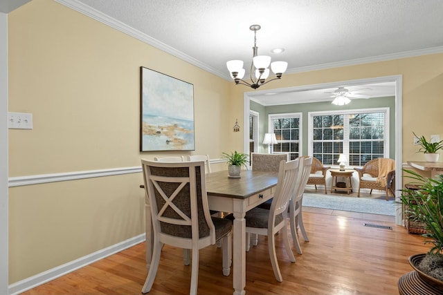 dining room with baseboards, light wood-style flooring, a textured ceiling, crown molding, and ceiling fan with notable chandelier