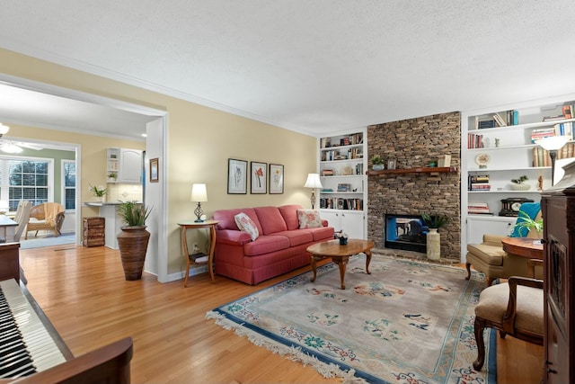 living room featuring light wood-type flooring, a fireplace, crown molding, and a textured ceiling