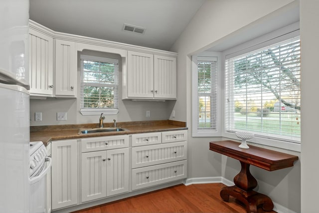 kitchen featuring electric stove, light wood finished floors, visible vents, white cabinetry, and a sink