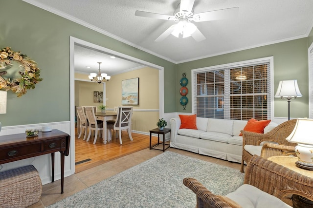 tiled living area with ornamental molding, a wainscoted wall, visible vents, and ceiling fan with notable chandelier