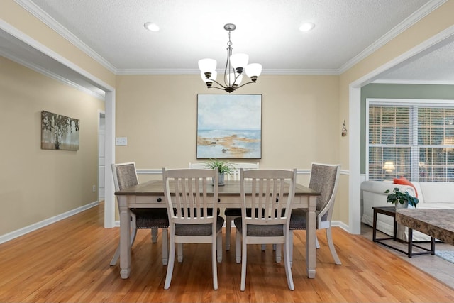 dining area featuring light wood finished floors, crown molding, baseboards, and a notable chandelier