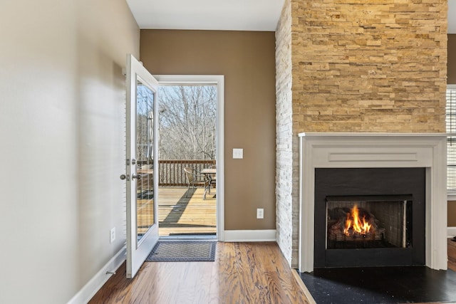 doorway with a warm lit fireplace, baseboards, and wood finished floors