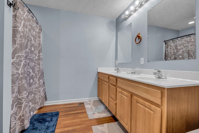 full bath with a textured ceiling, wood finished floors, a sink, and baseboards