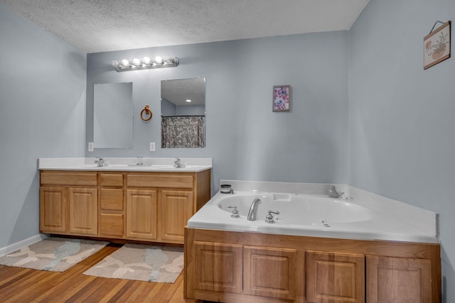 full bathroom with a sink, a textured ceiling, a tub with jets, and wood finished floors