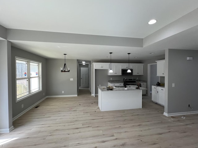 kitchen with light wood finished floors, black microwave, white cabinets, and a sink