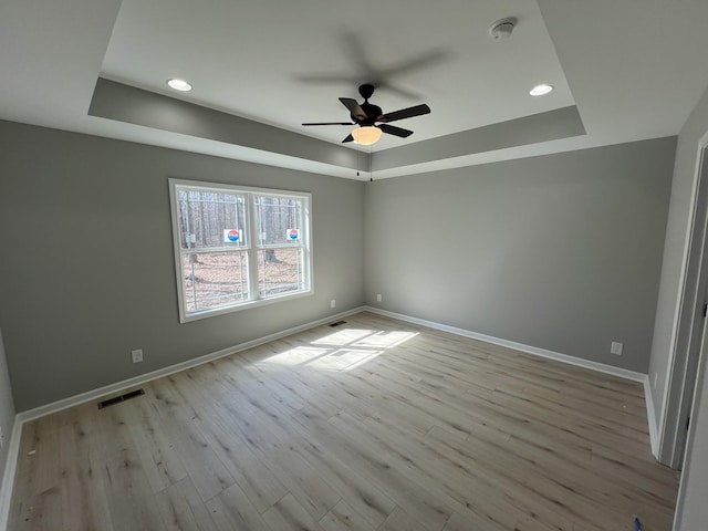 empty room featuring visible vents, a tray ceiling, and baseboards