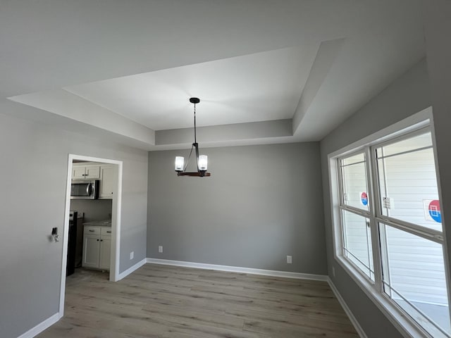 unfurnished dining area featuring a notable chandelier, a tray ceiling, light wood-style floors, and baseboards