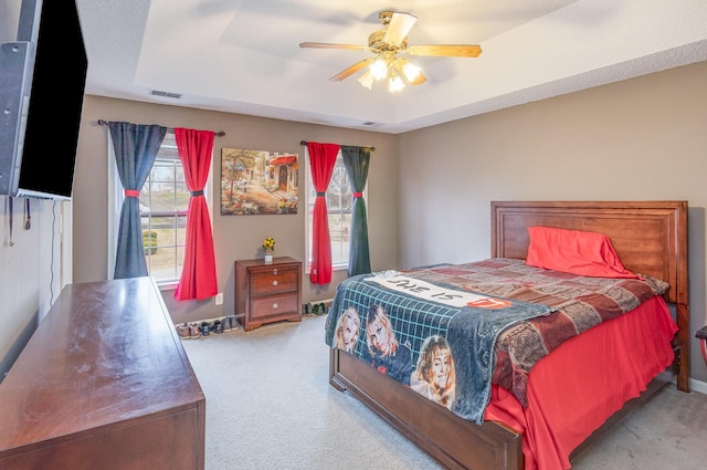 carpeted bedroom featuring a tray ceiling, visible vents, and ceiling fan