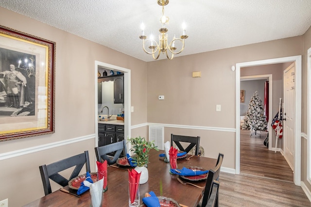 dining area with baseboards, visible vents, a textured ceiling, a notable chandelier, and light wood-type flooring