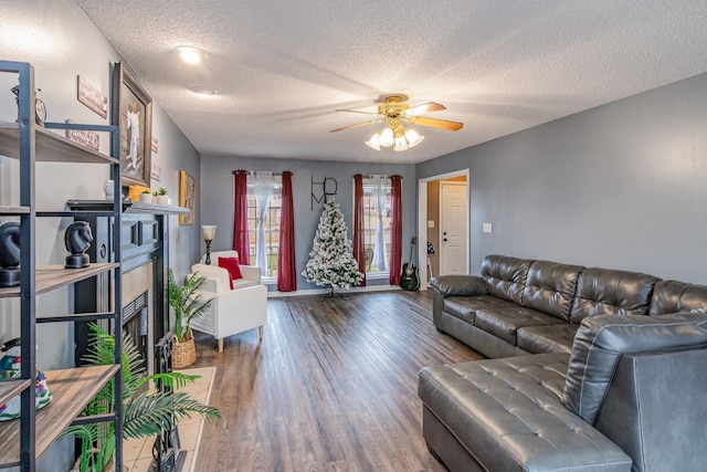 living room featuring a ceiling fan, wood finished floors, a fireplace, and a textured ceiling