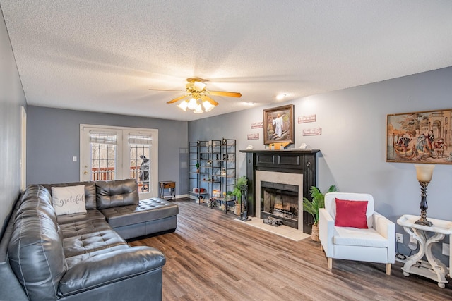 living room with a fireplace, a textured ceiling, ceiling fan, and wood finished floors