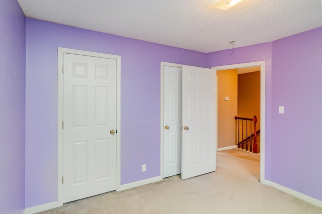 unfurnished bedroom with light carpet, a textured ceiling, and baseboards