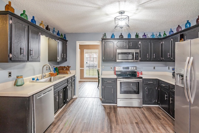 kitchen with a sink, a textured ceiling, wood finished floors, appliances with stainless steel finishes, and light countertops