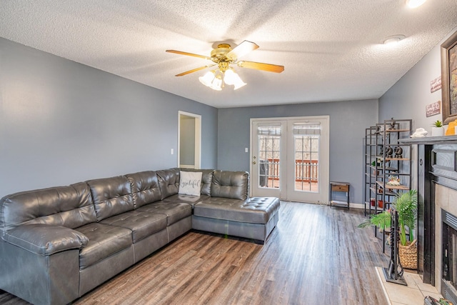 living room with baseboards, a tiled fireplace, wood finished floors, a textured ceiling, and a ceiling fan