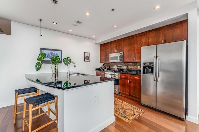 kitchen featuring light wood-style flooring, stainless steel appliances, a sink, visible vents, and backsplash