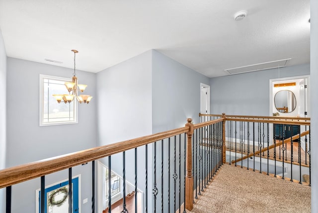 corridor featuring attic access, visible vents, an upstairs landing, and an inviting chandelier