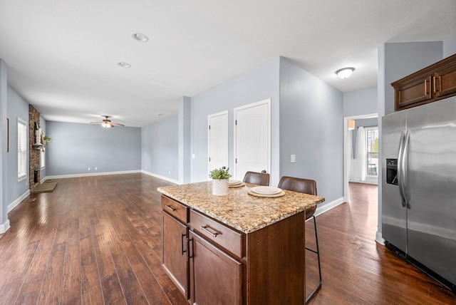 kitchen featuring a breakfast bar, baseboards, stainless steel refrigerator with ice dispenser, a center island, and dark wood finished floors