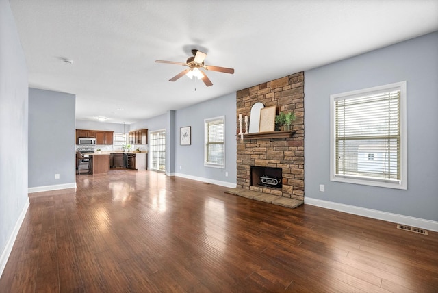 unfurnished living room featuring dark wood-type flooring, visible vents, a fireplace, and a ceiling fan