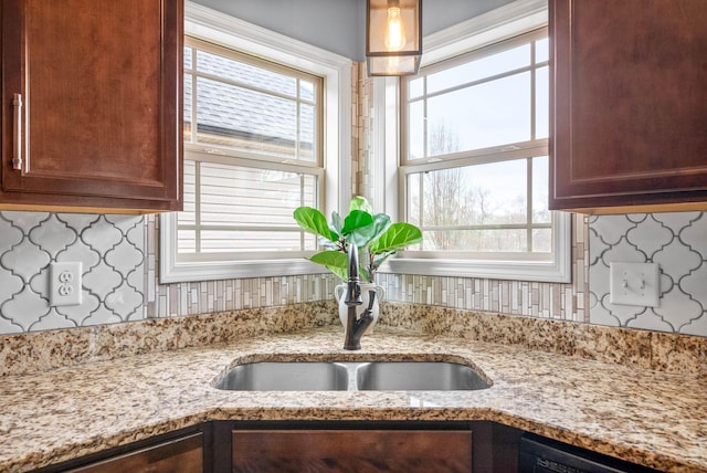 kitchen featuring dishwashing machine, tasteful backsplash, a sink, and light stone countertops